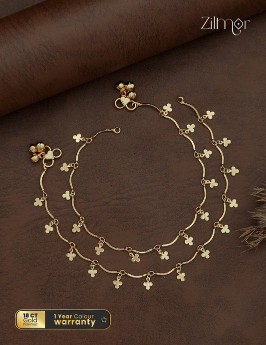 Zilmor 18K gold plated anklet pair with curved links, dangling clover-shaped charms and small bell-shaped accents.