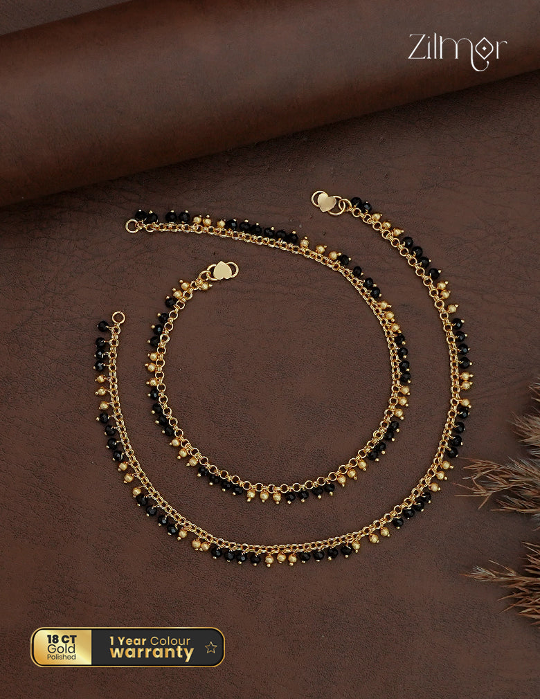 Matching black crystal bead anklet pair with gold-toned chains displayed on a brown background