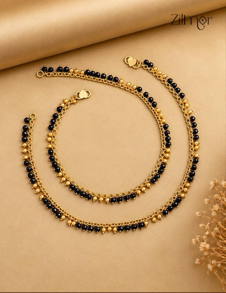 Pair of 18K gold plated anklets with black crystal beads and gold-toned bead accents on a beige background