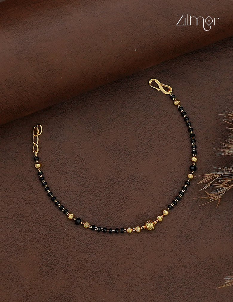 Black bead mangalsutra bracelet with gold-plated centre bead displayed on a beige roll