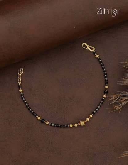 Black bead mangalsutra bracelet with gold-plated centre bead displayed on a beige roll