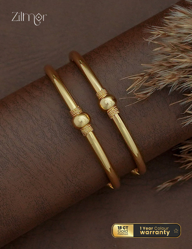 Zilmor 18K gold plated slim bangle pair with rounded centre accents and rope-textured detailing on a brown display.