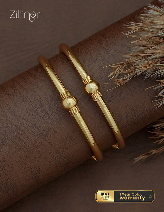 Zilmor 18K gold plated slim bangle pair with rounded centre accents and rope-textured detailing on a brown display.