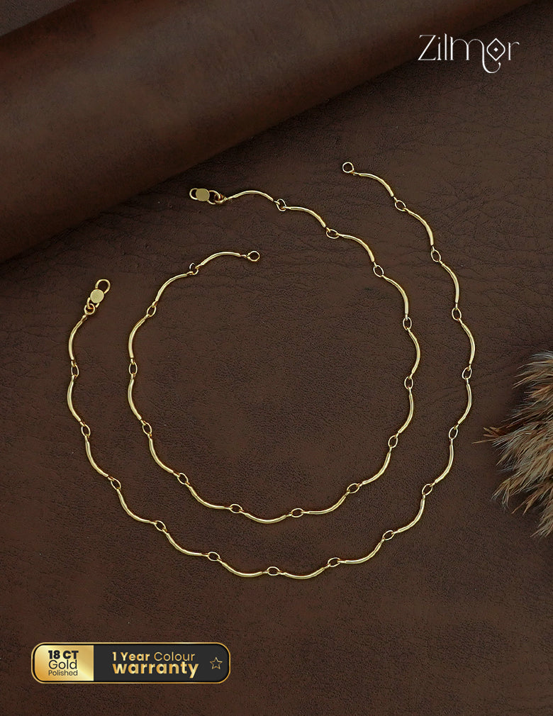 Zilmor 18K gold polished anklet pair with curved chain links and lobster-claw clasps on a brown background