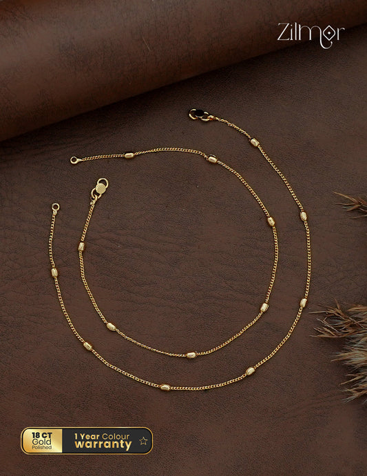 Zilmor gold-tone chain anklet pair with spaced oval beads and clasp closures, arranged on a brown background.